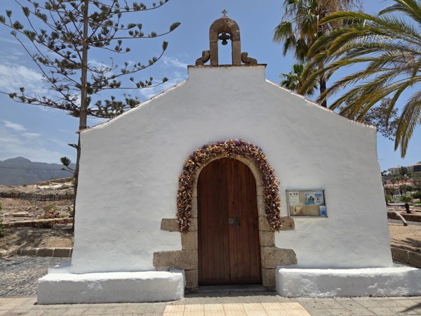 Whitewashed Ermita de la Encarnación chapel with wooden door and bell.