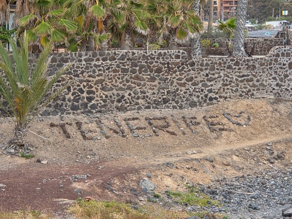 The word 'TENERIFE' formed with beach stones beside a lava-stone wall.