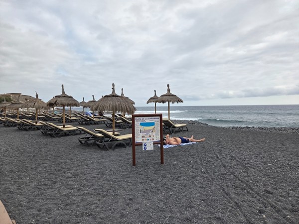 Dark pebble sands and thatched umbrellas at Playa de La Enramada.