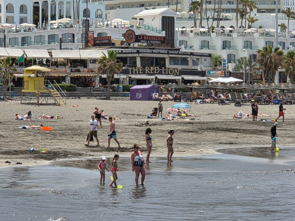 Families wading at Playa Fañabé with restaurants and lifeguard tower behind.