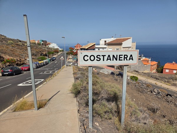 Entrance sign reading COSTANERA on a hillside street with the Atlantic visible in the background.