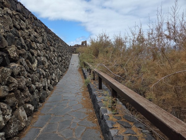 Narrow stone walkway with timber handrail hugging the cliff at Costa El Sauzal.