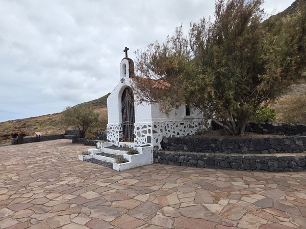Small white chapel called Ermita de Las Rojas set on a stone terrace near the coastal path.