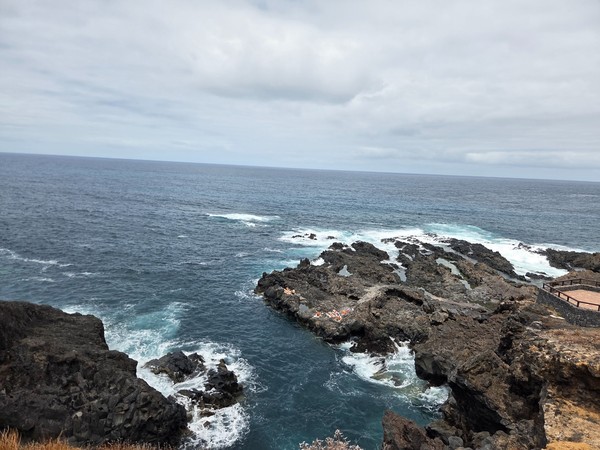 Sunbathers on a narrow lava platform with Atlantic waves breaking around natural basins below the cliffs.