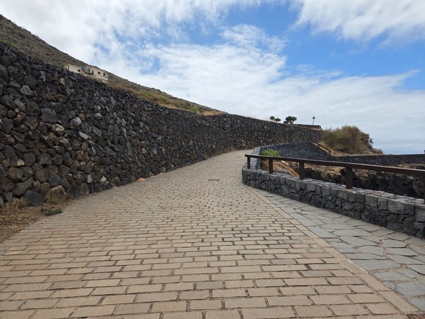 Curving lane leading toward the abandoned building, edged by volcanic scrub and stone walls.