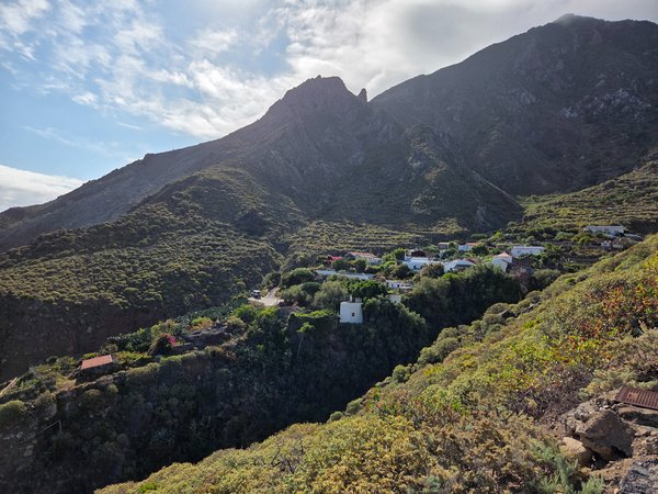 Panoramic shot of Draguillo hamlet tucked beneath jagged Anaga peaks, surrounded by terraced slopes and lush vegetation.