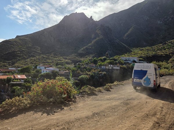 Dusty track leading into Draguillo with an Emmasa service van kicking up dust against a backdrop of steep green mountains.