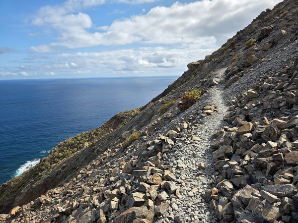 Stone-paved footpath clinging to a scree slope high above the ocean on the rugged trail between Draguillo and Chamorga.