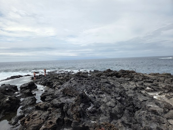 Closer panorama of El Marquéz with bathers standing on the rocks beside the natural pools.