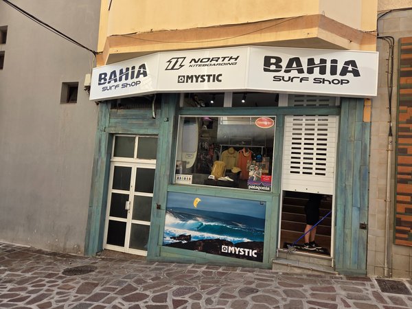 Facade of Bahía Surf Shop selling kitesurf and windsurf gear, painted in ocean-inspired turquoise tones.