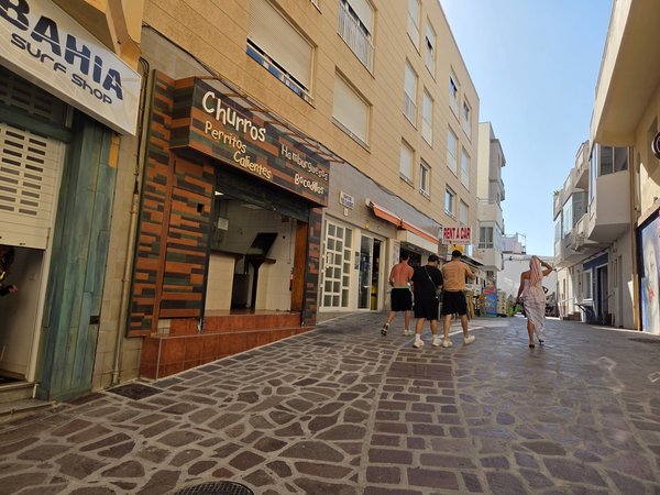 Friends leaving the beach via a stone-paved alley lined with churro stands, rental desks and tiny tapas bars.
