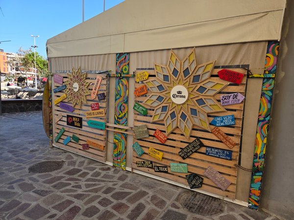 Vibrant Corona-themed pop-up wall covered with hand-painted wooden signs quoting island slang.
