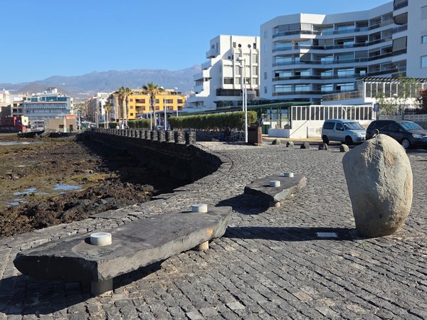 Basalt-paved jetty with minimalist benches overlooking the bay and the Guajara mountains.