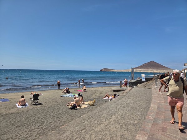 Sunbathers relaxing on the dark volcanic sand of Playa de El Médano with Montaña Roja rising behind.