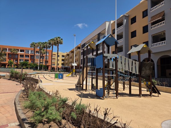Modern playground framed by colourful apartments and tall palm trees—ideal for families.