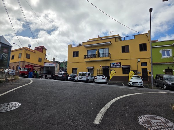 Yellow residential building with wooden balcony and green garage door on a quiet street.