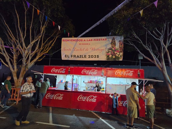 Banner welcoming visitors to the Fiestas de El Fraile 2025 in honor of Santa Isabel de Portugal above a refreshment kiosk.