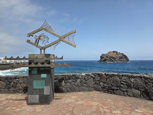 Metal fish sculpture on Garachico's seafront with Roque de Garachico in the background.