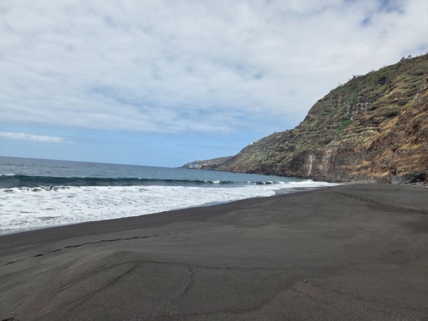 Wide panoramic view of Playa de Garañona with open Atlantic waves and a long strip of black volcanic sand below high cliffs.