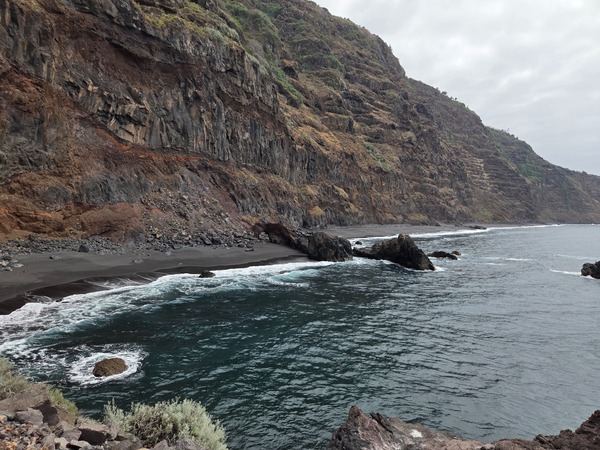 View along the cliff-backed coastline at Garañona showing multiple coves and black-sand pockets broken by rock promontories.