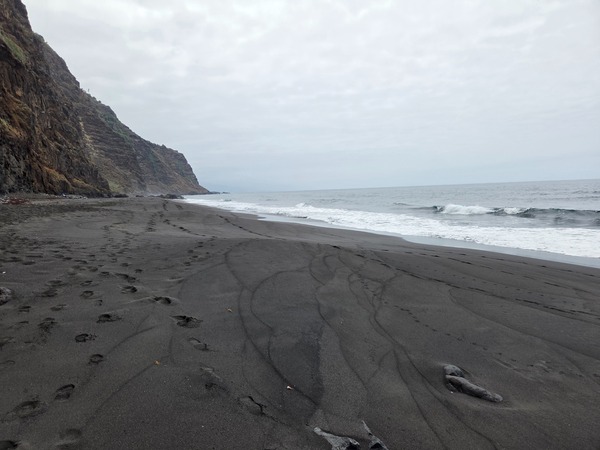 Close view of the fine basaltic black sand at Playa de Garañona with footprints and subtle flow lines.