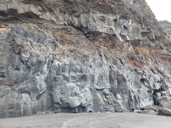 Natural lava arch and boulder field at Playa de Garañona beneath layered basalt cliffs.