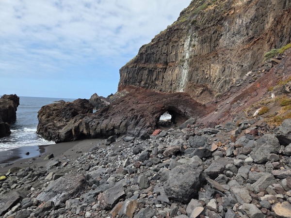 Sheer cliff at Garañona showing grey columnar lava and weathered layers stacked above the beach.
