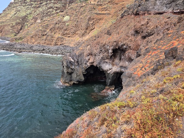 View from the access path showing a sea cave and turquoise water below the lava ledges.