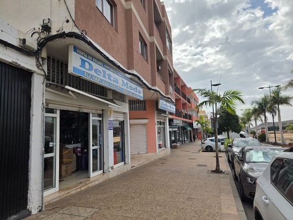 Row of fashion and accessory shops in Guaza Tenerife with the Delta Moda sign and palm trees along the pavement.