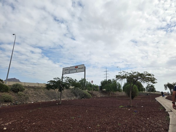 Road sign by the TF-66 showing directions to Guaza and Valle San Lorenzo with volcanic soil and low trees around.