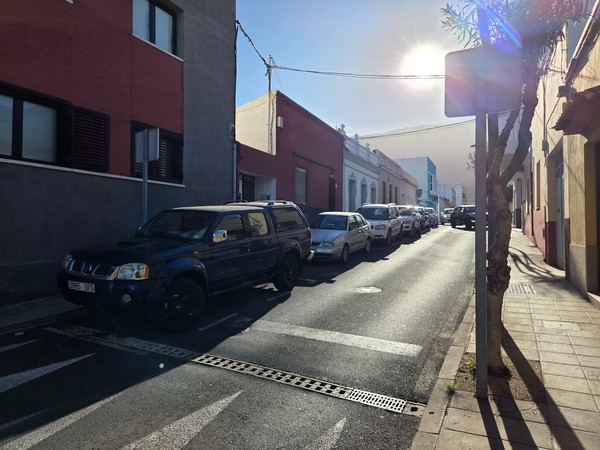 Narrow residential street in Güímar with parked cars and low houses under the afternoon sun.