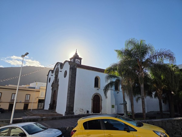 Side view of the church of San Pedro Apóstol in Güímar with palm trees and a yellow car in the foreground.