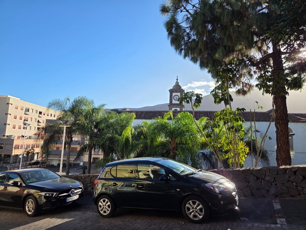View towards the church clock tower in Güímar framed by palm trees and parked cars on a sunny afternoon.