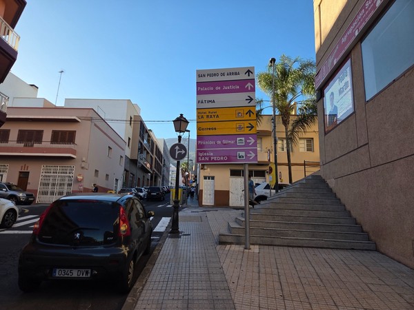 Set of pink and yellow direction signs in Güímar indicating routes to the justice court, post office and church of San Pedro.