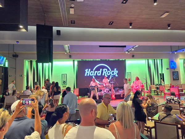 Live band performing on the Hard Rock Cafe Tenerife stage with the large Hard Rock logo behind the drummer.