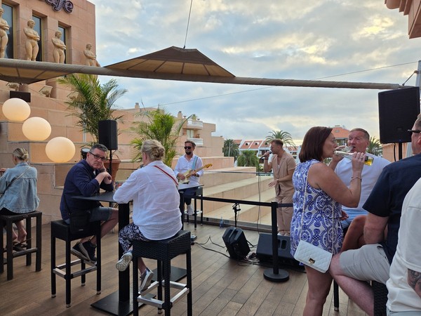 Musician singing at the Hard Rock Cafe Tenerife rooftop terrace during sunset with guests at high tables.