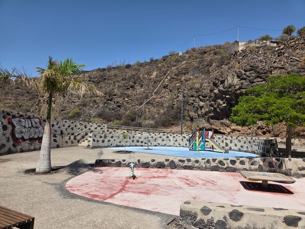 Children’s playground with slide and soft flooring set against a volcanic rock wall inside La Higuera park.