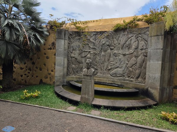 Bas-relief fountain and bust honouring botanist amid palm courtyard.