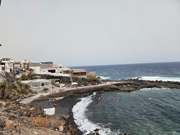 Elevated view of the main bathing platform and natural cove at La Caleta de Punta Prieta with swimmers and volcanic shore.