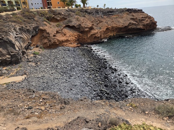 Overhead view of the black-pebble beach at Playa Las Salinas surrounded by red volcanic cliffs.
