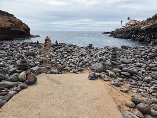 Small stone cairns arranged on a concrete platform among rounded pebbles at Playa Las Salinas.