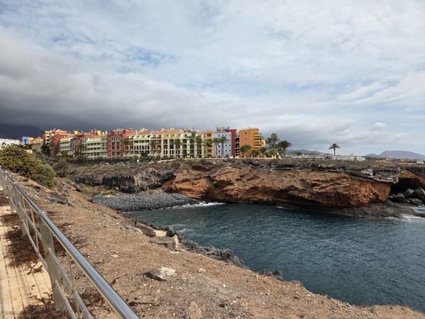 Panoramic view of Playa Las Salinas cove in Costa Adeje, with lava cliffs, calm Atlantic water and colorful buildings on the promenade.