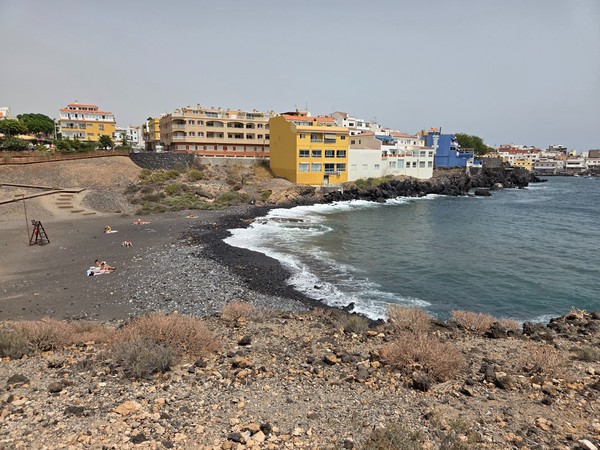 Black-sand beach bordered by yellow and blue buildings in Los Abrigos Tenerife.
