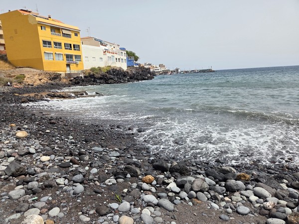 Close-up of the pebble and black-sand shoreline in Los Abrigos with gentle Atlantic waves.