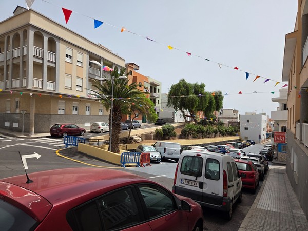 Decorated streets of Los Abrigos with festive bunting above parked cars.
