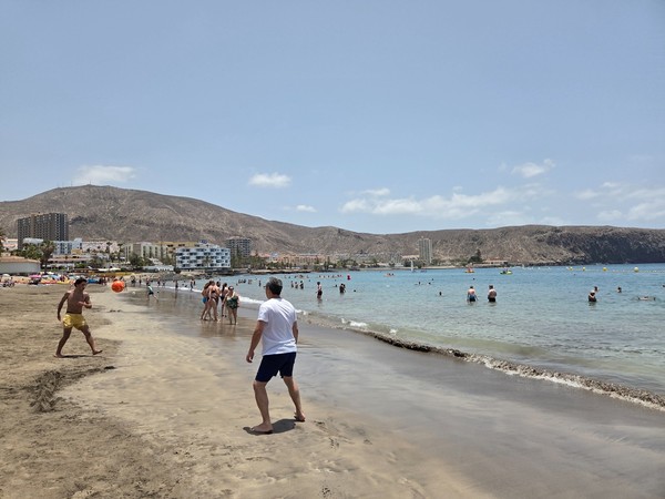 Two men playing ball on the wet sand at the waterline of Playa de Los Cristianos while swimmers enjoy the calm bay.