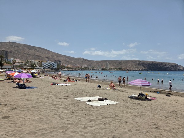Holidaymakers relaxing on towels and under colourful umbrellas on Playa de Los Cristianos in Tenerife.
