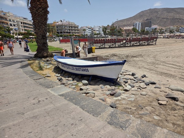 Decorative fishing boat with the words Bahia Playa Los Cristianos displayed beside the promenade and the sandy beach.