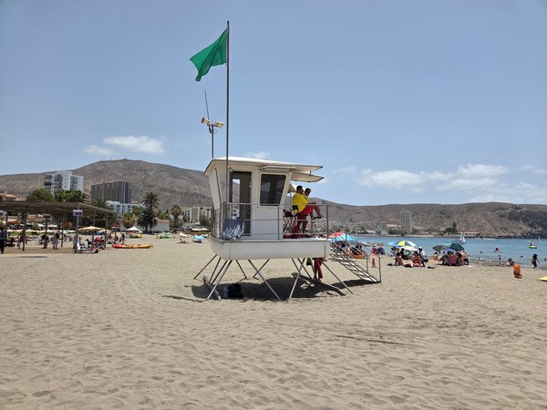 Lifeguards watching over Playa de Los Cristianos from a raised tower with a green safety flag flying.