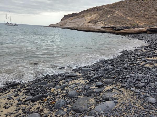 Rocky shoreline of Playa de los Morteros with dark volcanic stones and cliffs in the background.